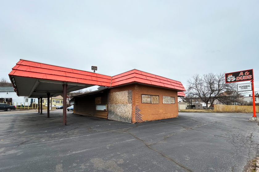 A brown building with an orange roof has particle board covering its windows.
