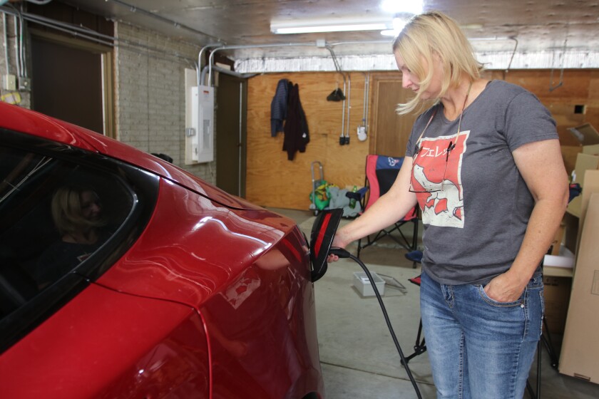 A woman in a gray graphic T-shirt plugs in a red electric car.