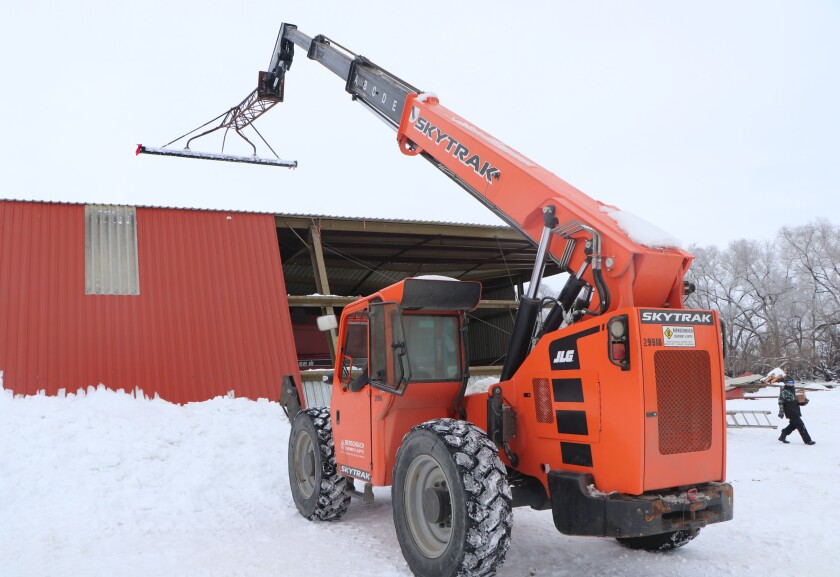 A telescopic handling machine is equipped with a makeshift snow rake/wiper, attempting to remove snow from a roof.