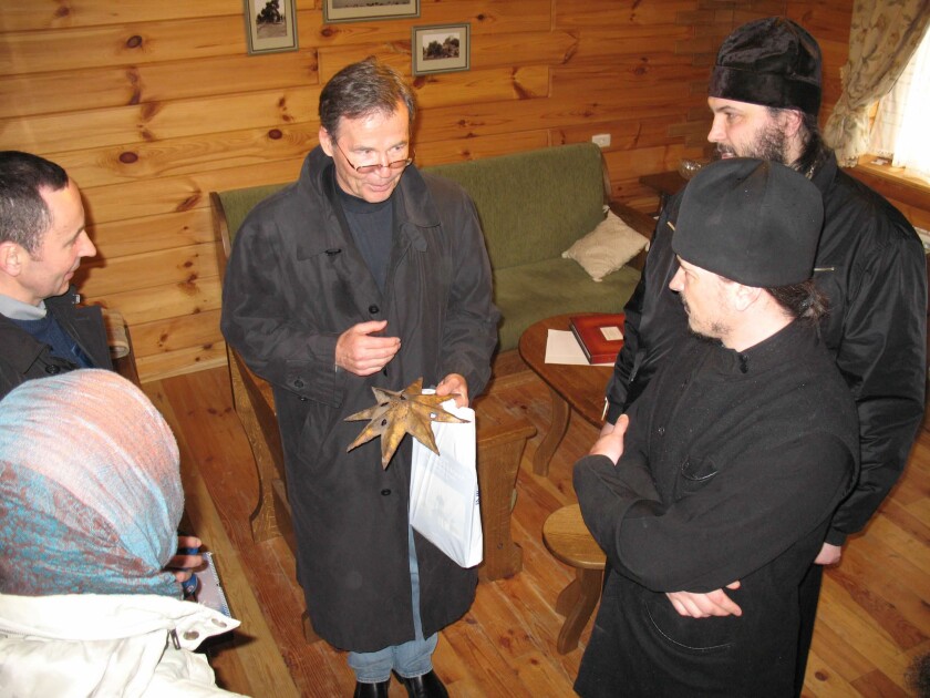 Howard Dahl, standing among Russian Orthodox clergy in a cabin-like building, accepts a bullet-ridden metal star from a monastery that had been desecrated by Soviet troops in 1930.