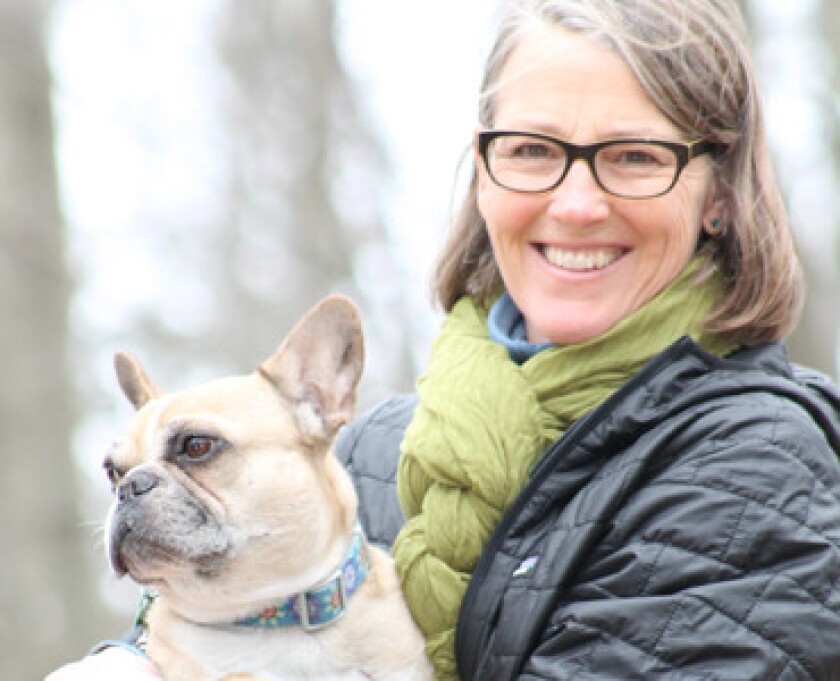 Dr. Jean Larson smiles with her French bulldog, with nature in the background.