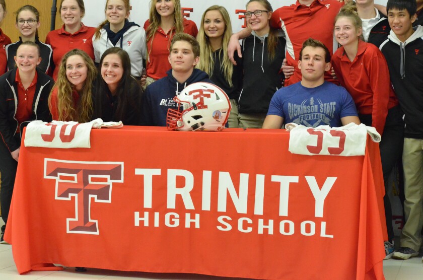 Surrounded by classmates, coaches and teachers, Dickinson Trinity seniors Logan Karsky (left) and Hunter Dassinger (right) celebrate joining the DSU football program on Wednesday, Jan. 24. (Shelby Reardon / The Dickinson Press)
