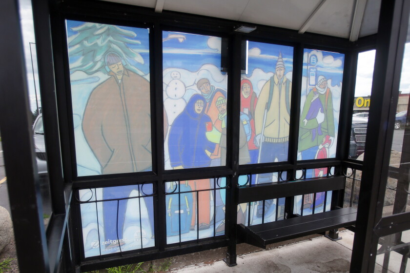 A bus shelter with windows decorated with a mural featuring a winter scene.