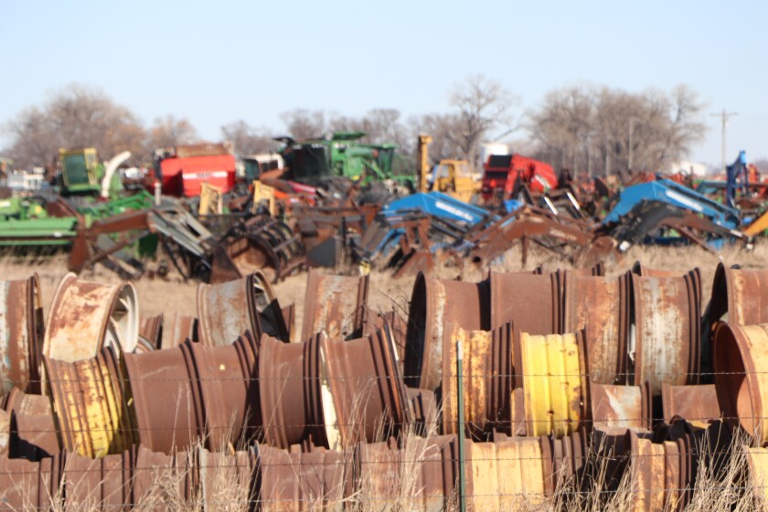 Rusting tire rims in the foreground are flanked by salvage ag machines covering more than 100 acres.