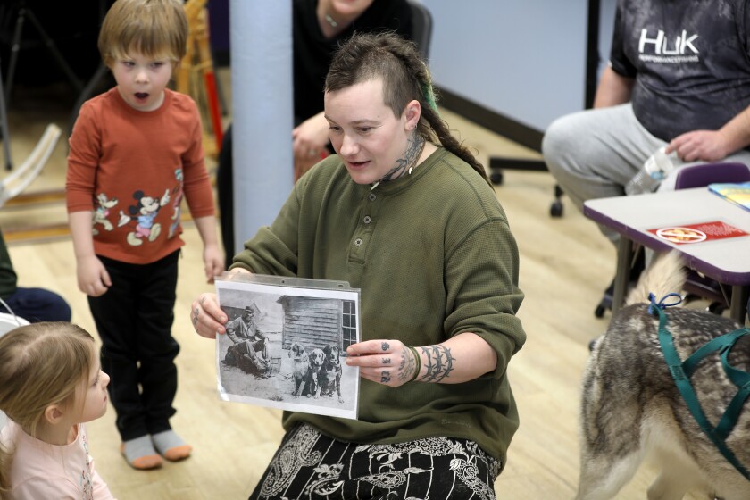 A person holds up a historic photograph while speaking at a children's event.