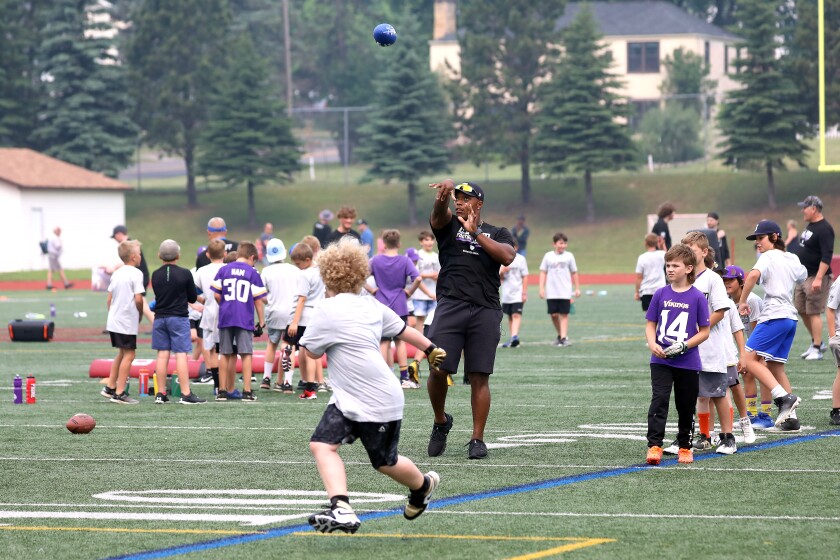 A pro football player throwing the ball to a young kid during a camp.