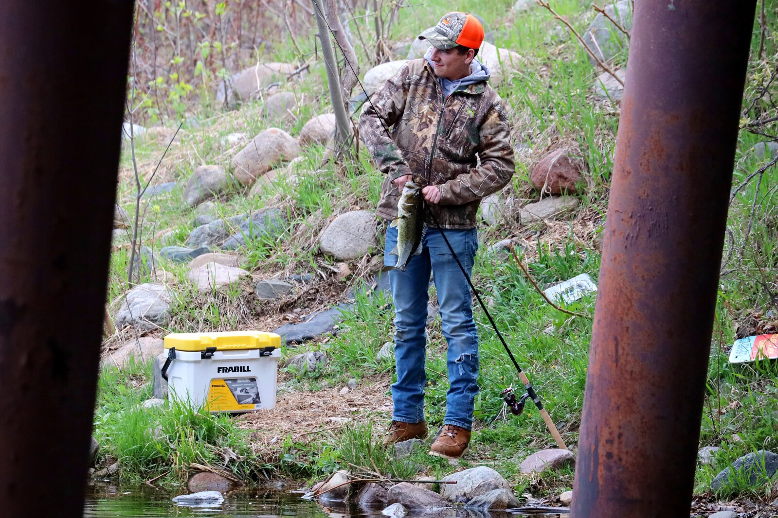 An angler takes a bass off the hook while standing on the shoreline.