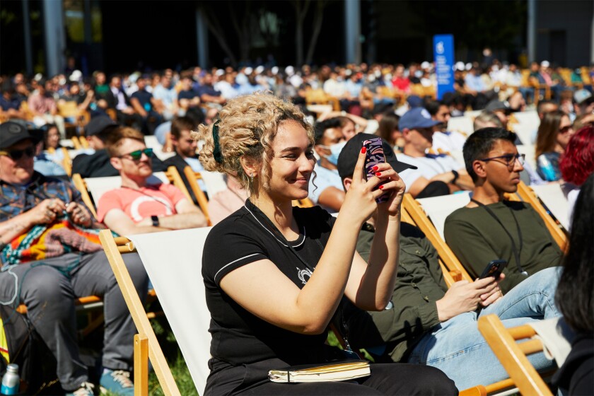 People sit outside in the sunshine in rows of chairs.