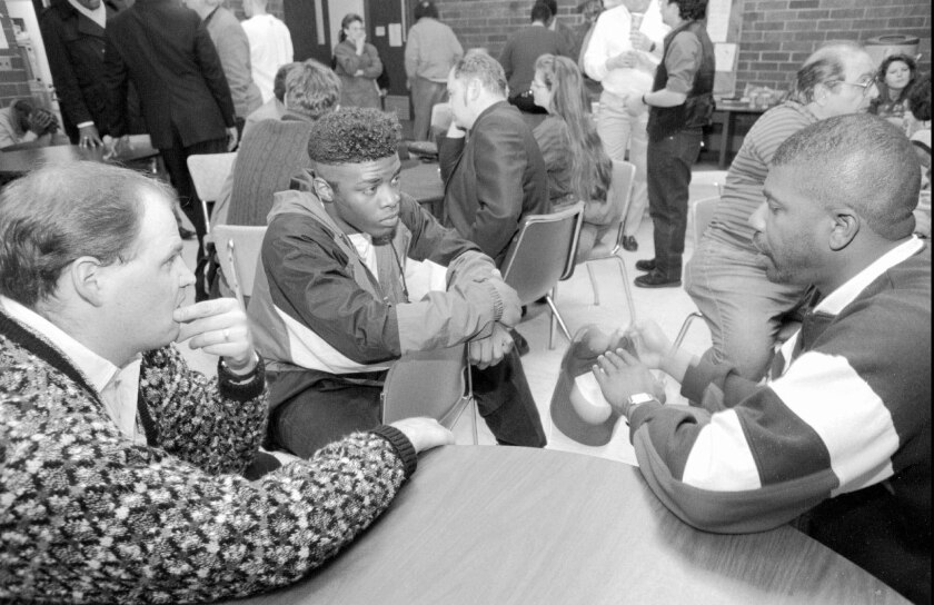 black and white photo of three men in discussion around table