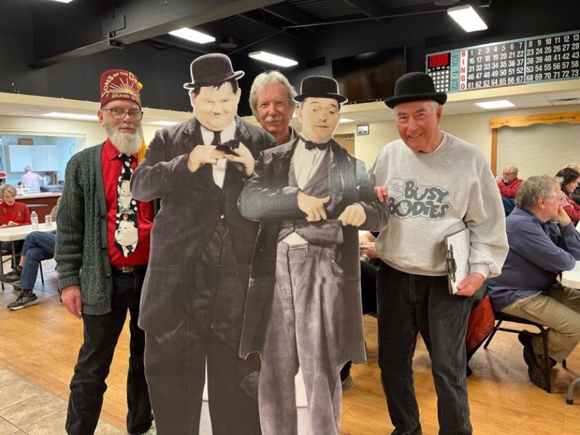 Three men pose with a large black and white cardboard cutout of Laurel and Hardy.