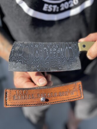 A meat cleaver, made by Cody Adolphson for the 10th Annual Bakken BBQ auction, pictured above, features 40 layers of 1095 steel and pure nickel, featuring a G10 handle.