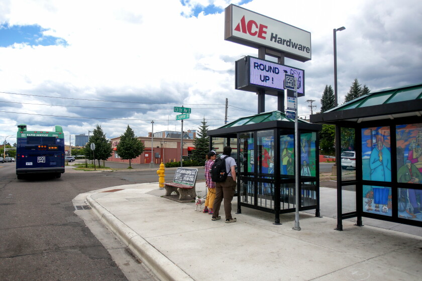 People standing near bus shelters decorated with murals as a bus travels away in the distance.