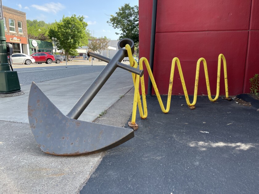 A bike rack in the shape of a yellow zig-zag chain attached to a large anchor.