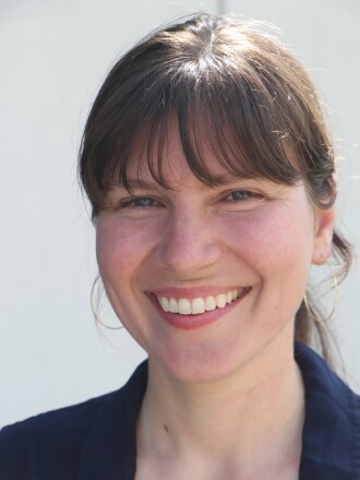 A smiling brown-haired woman stands against a white backdrop.