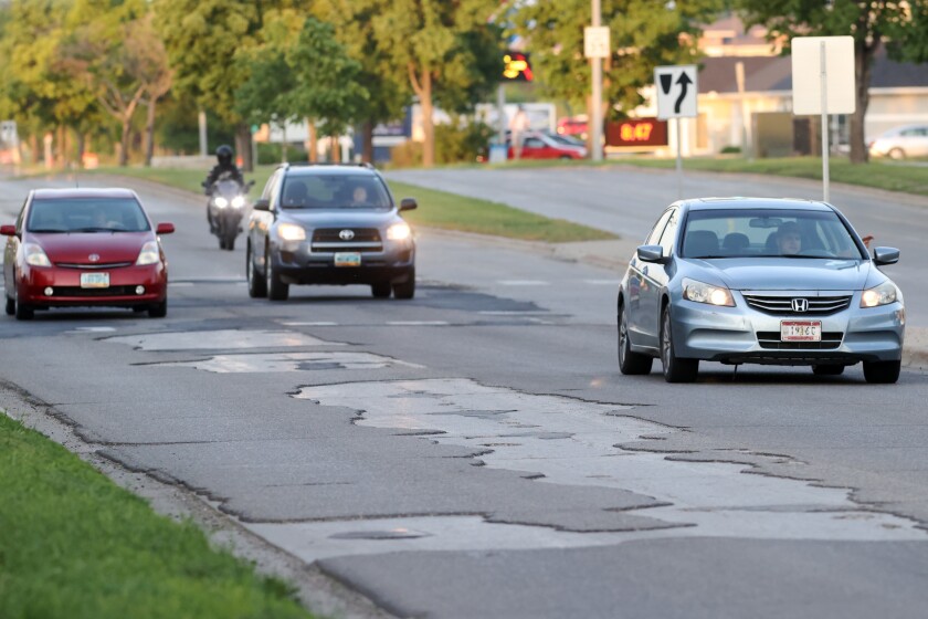 Cars and a motorcycle drive down an uneven stretch of road.