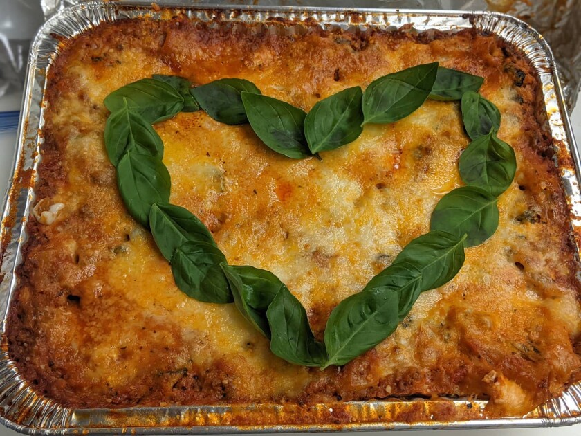 A lasagna topped with an outline of a heart made with basil leaves