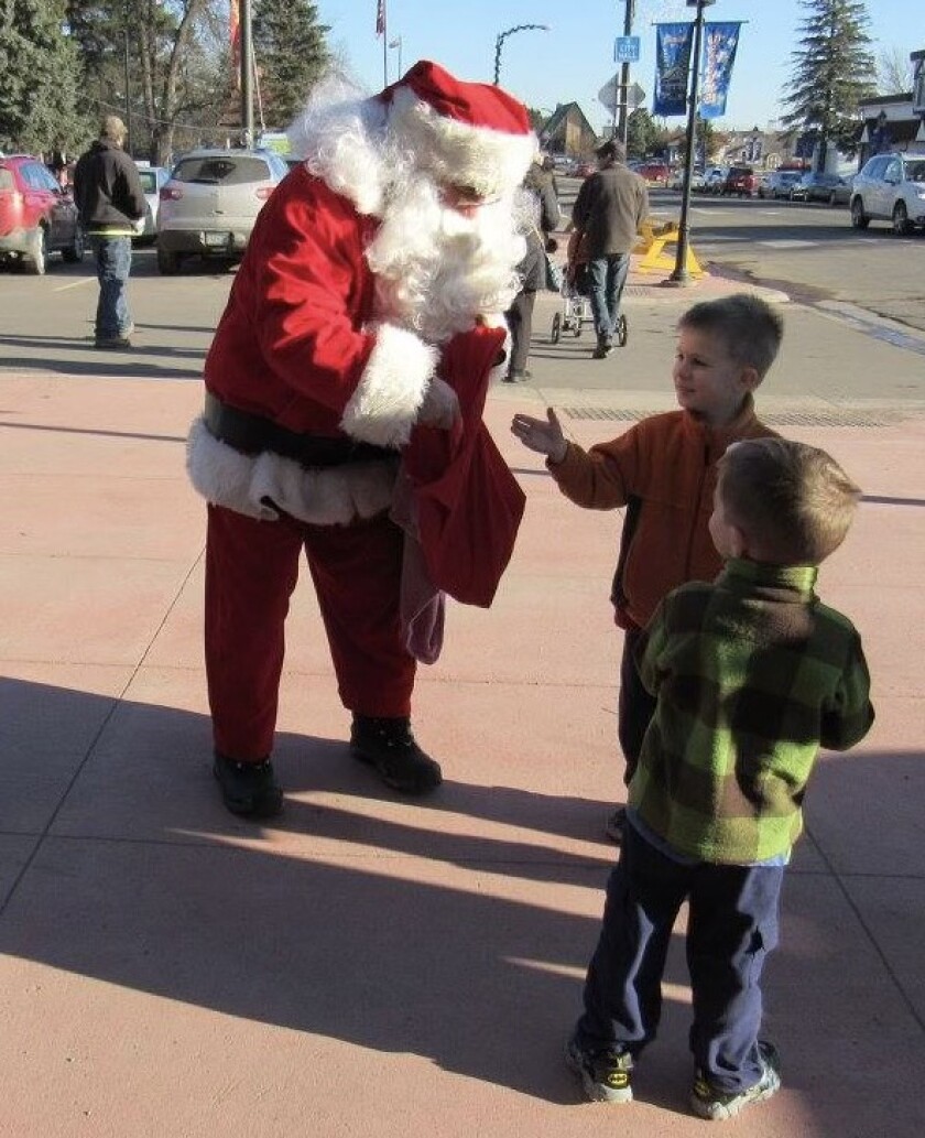 Santa Claus digs in his bag for a gift for two young boys.