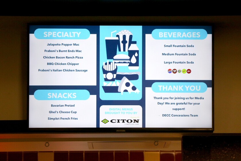 A digital menu screen inside of an arena with food items listed.