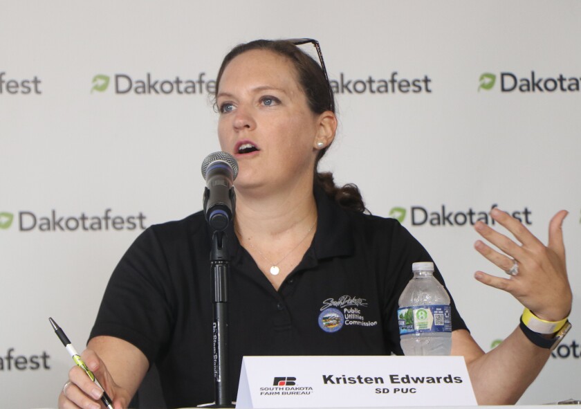 A woman lawyer with glasses on her head, gestures as she answers questions on a farm show educational panel stage.