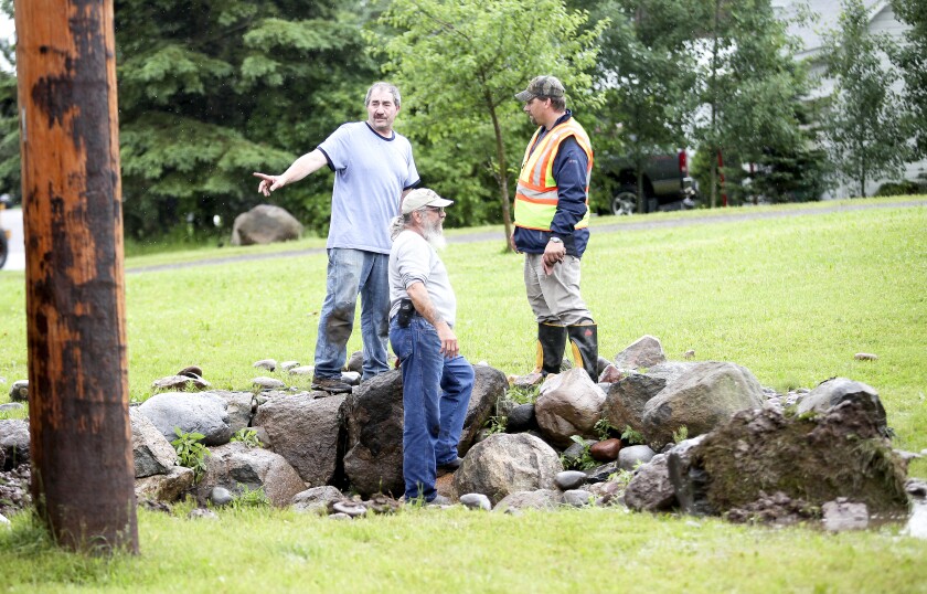 Three men gesture while speaking on a large pile of rocks