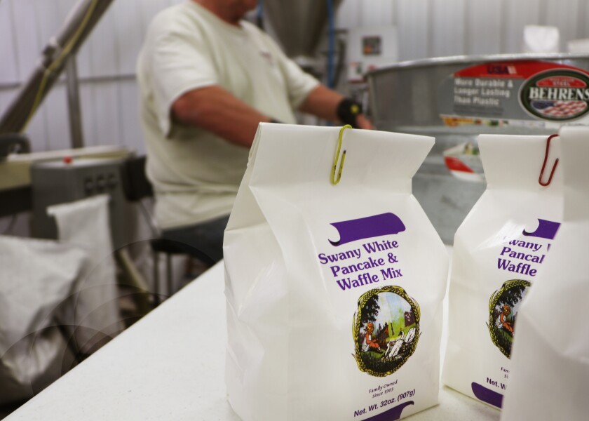 Packages of Swany White Flour mix stand on a table as the miller packs them.