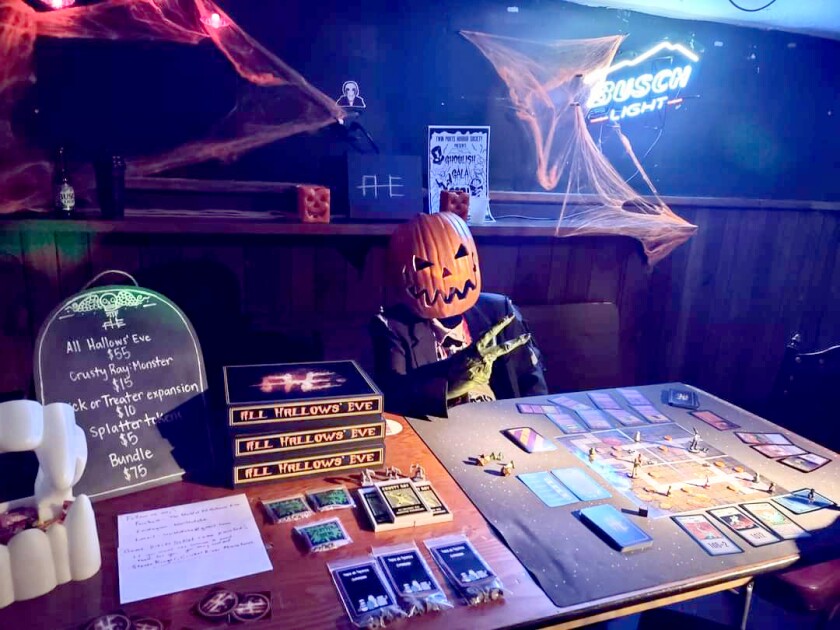 A person dressed with a pumpkin head costume sits at a table with a board game on it.