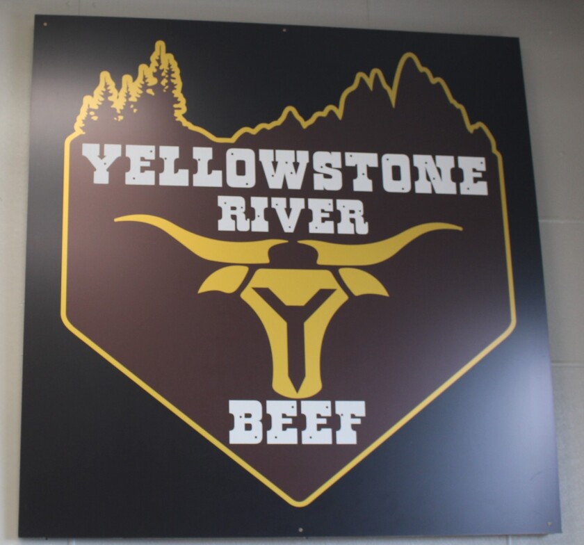 A brown, white, yellow and black Yellowstone Beef sign hangs on a wall.