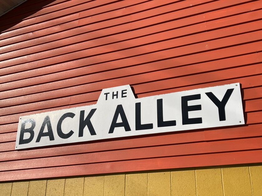 A black-on-white sign reads THE BACK ALLEY, posted against orange-painted horizontal siding with some yellow-painted vertical siding visible below.