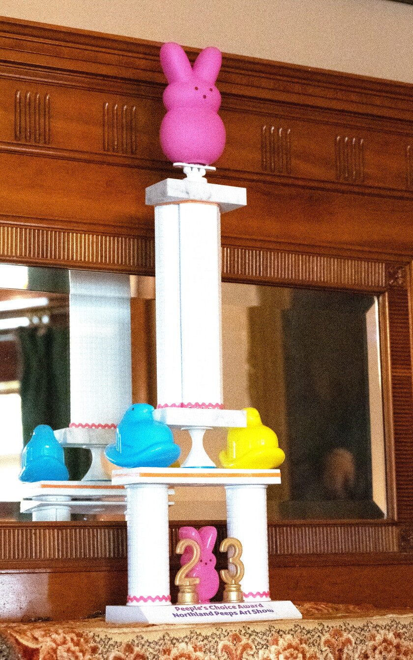 A white multi-tier trophy is adorned with pink, blue and yellow figures resembling Peeps candies. Gold numerals 2 and 3 are mounted at base.