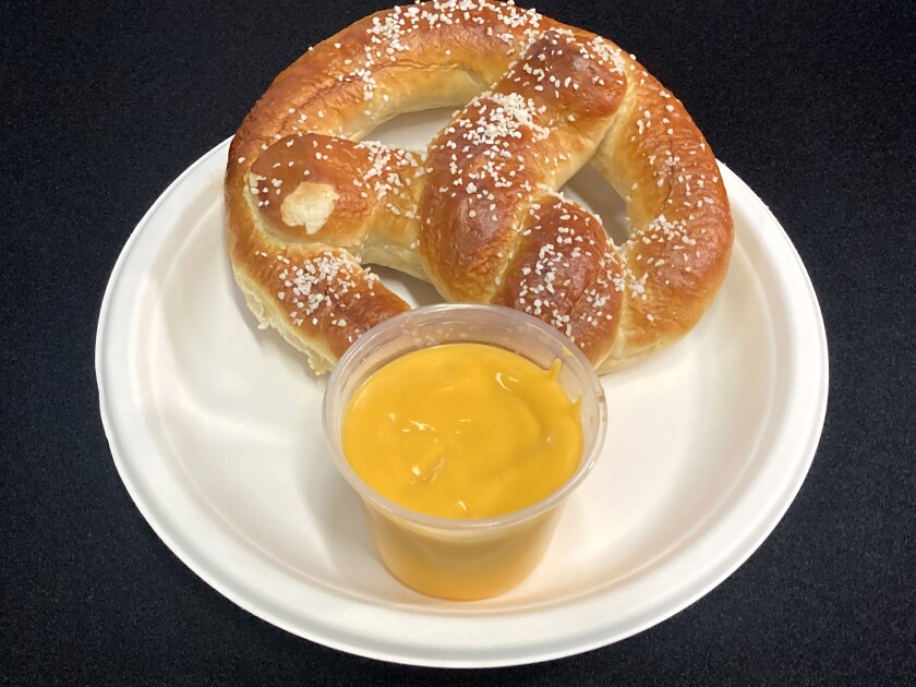 A Bavarian pretzel on a plate with nacho cheese in a plastic cup.