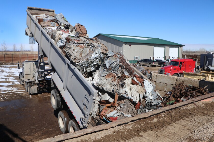 A long semi-trailer lifts up from left to dump crushed ag parts and other recyclable scrap metals to be loaded onto rail cars.