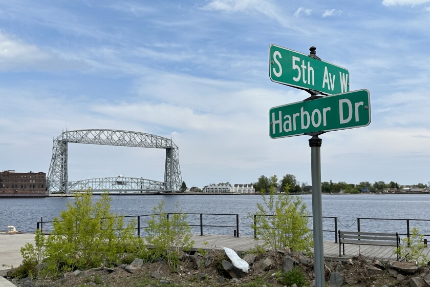 Street signs indicate the intersection of S. 5th Ave. W. and Harbor Dr. Duluth Harbor is visible in background, with Aerial Lift Bridge.