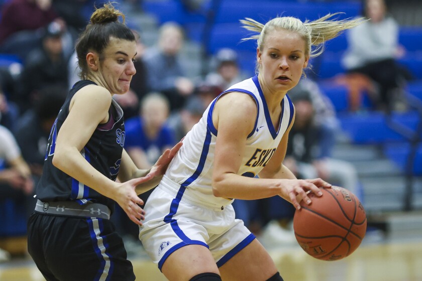 Girls basketball players in black uniforms compete against players in white uniforms at a high school gymnasium.