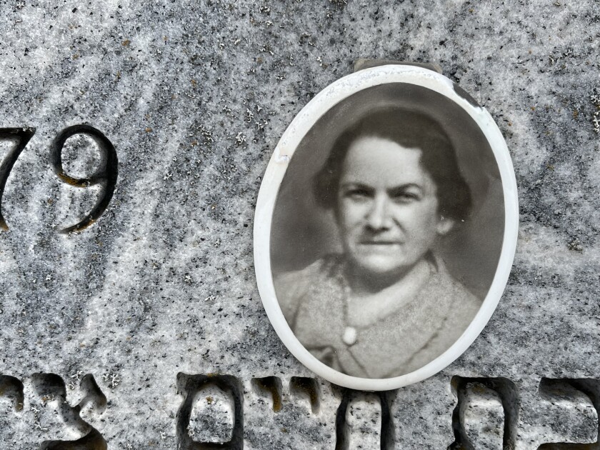 Close-up view of gravestone featuring blurry black-and-white photo of middle-aged woman. Numbers and Hebrew lettering indistinctly visible at edges of photograph.
