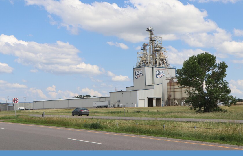 A black car drives to the left on an Interstate Highway, with the Famo Feeds feed mixing and pelleting factory in the background.