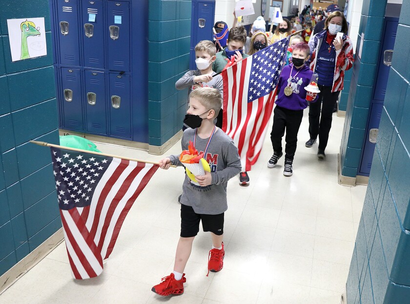 Logan Shuster, front, is followed by his brother, Luke, as they hold United States flags, just like their dad, John Shuster, did earlier in the day in Beijing, while they lead classmates in an opening ceremony parade at Great Lakes Elementary School