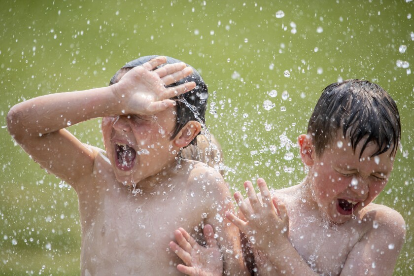 Beaude Schultz, 7, from left, and Jasper Halverson, 7, react to water pouring on their heads while attempting to beat the heat as temperatures hit 90 degrees at the splash pad located at Rice Park in Willmar on Tuesday, June 14, 2022.