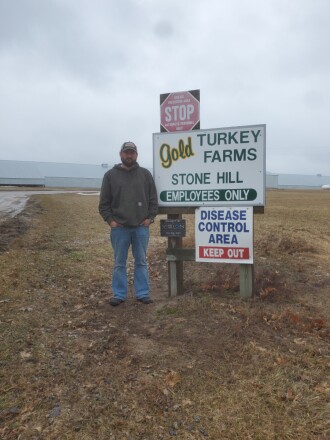 Derekas Goldas iš Gold Turkey Farms stovi šalia Motley įsikūrusios įmonės iškabos