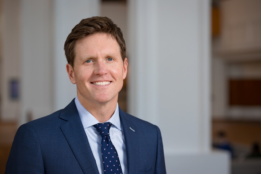 Joe Bloodgood is a man wearing a blue suit paired with a blue tie with pink polka dots, smiling into the camera.
