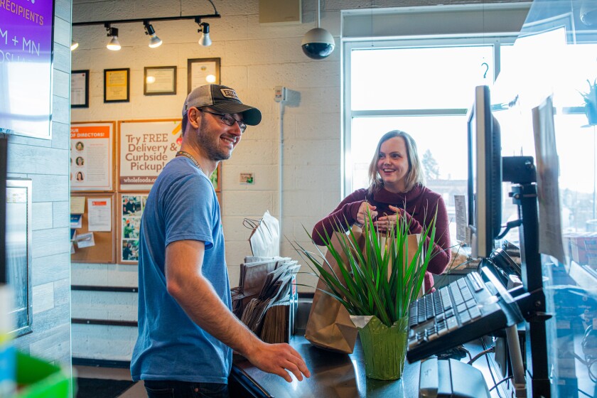 Aaron Peterson looks at a cash register behind the counter as Josephine Lepak lifts paper bags at the Whole Foods Co-op Hillside location.