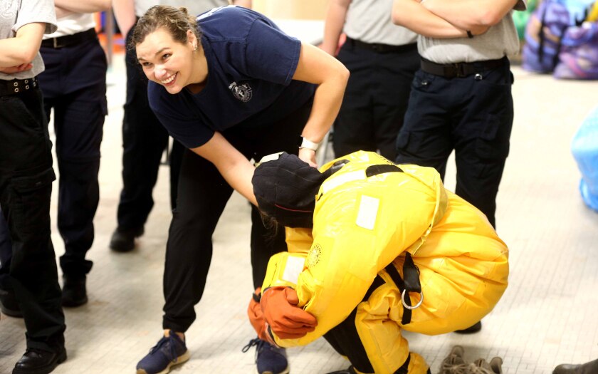Firefighter smiles while helping a student put on a water rescue suit