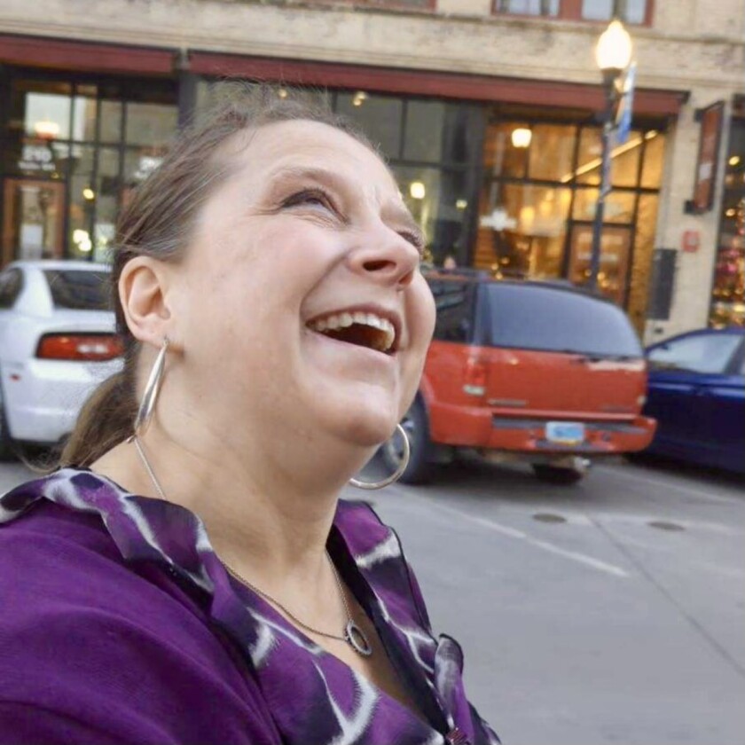 A closeup photo of a smiling woman's face. She's wearing a purple top and hoop earrings.