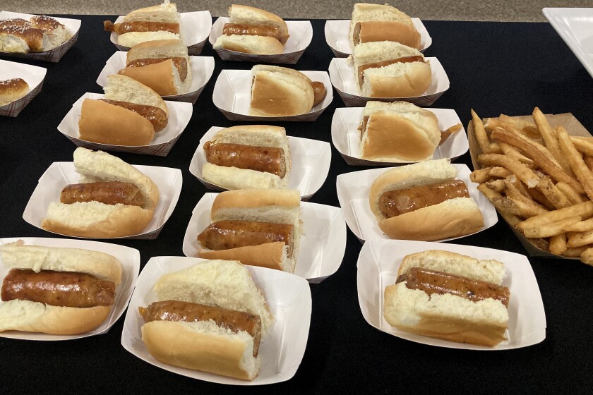 Paper trays containing Italian chicken sausage on buns and a paper trey containing French fries.