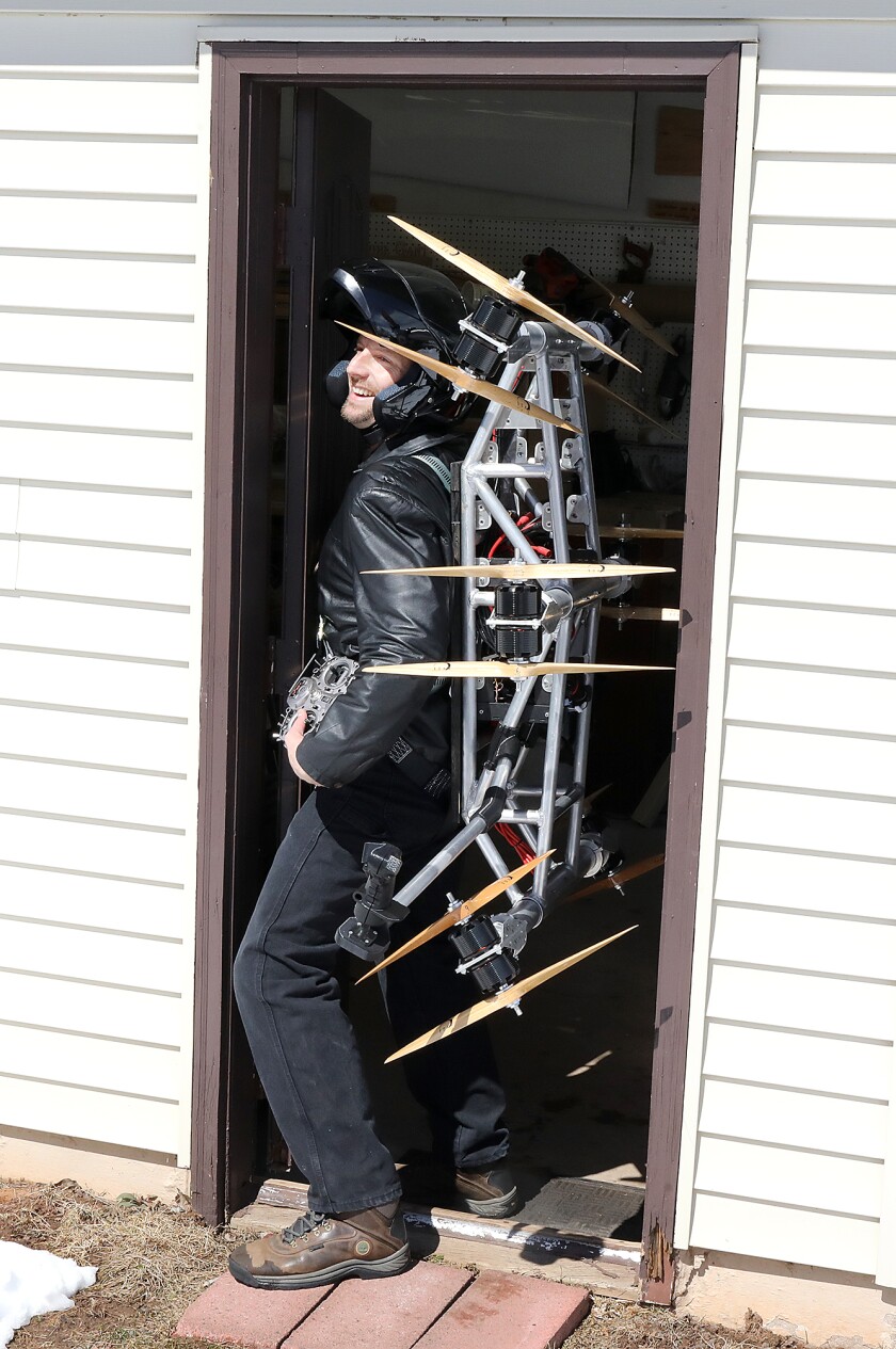 Ascend Dynamics, LLC founder, Daniel Gant, smiles as he wears the prototype of his SkyPak, a propeller-driven jetpack, on his back while getting through the door of his workshop