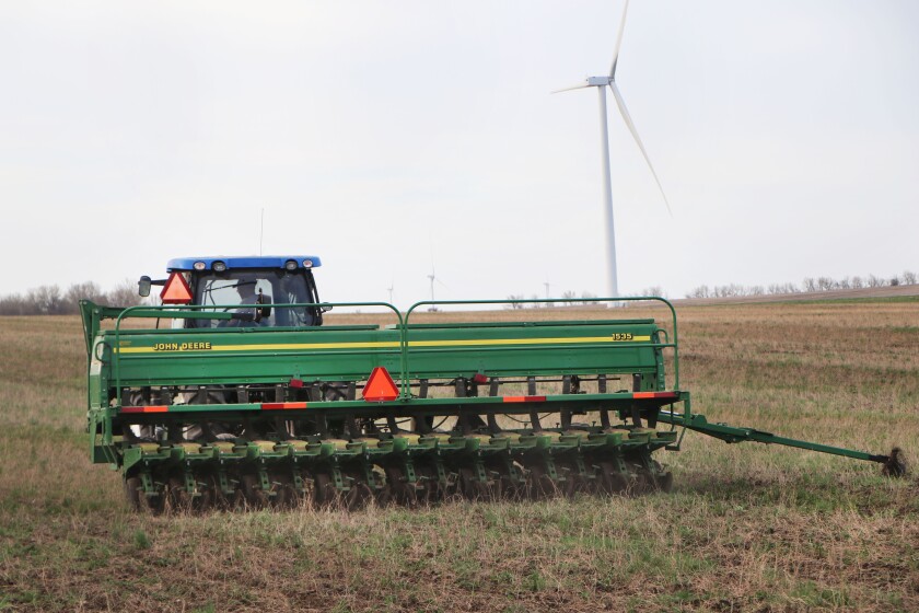 A planter with an old-school marker wheel goes moves across a field, planting soybeans into an alfalfa field.