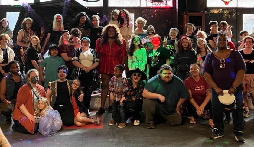 A large crowd of people of ages varying from young children to adults, some colorfully costumed, pose for a group photo.