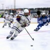 A high school boys hockey player controlling the puck during an outdoor game.