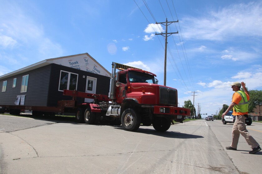 A man in a yellow vest directs a semitractor-trailer pulling a house into the road from the Fargo North parking lot.