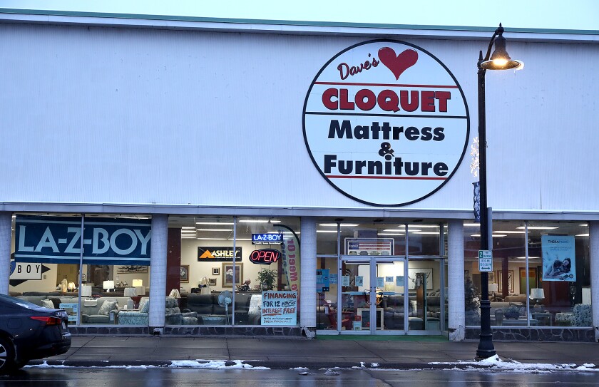 The lights are on inside of Dave’s Cloquet Mattress & Furniture on Cloquet Avenue as the light fades outside
