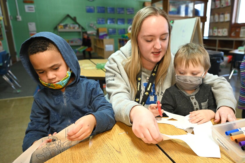 Two children cutting paper with teacher at preschool